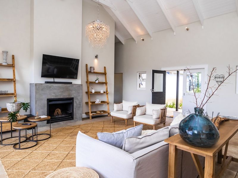 Spacious living room featuring a vaulted ceiling with exposed rafters, a modern concrete fireplace, and tiled flooring with direct access to the outdoors.