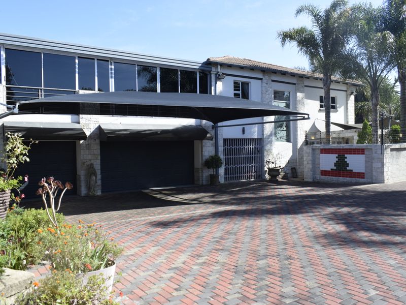 Front elevation of a multi-story house featuring a paved driveway, large shade sail, stone facade, and integrated garage doors.