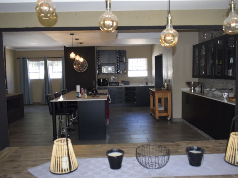 Spacious open-plan kitchen and living area featuring modern dark cabinetry, a central island with breakfast bar seating, and contemporary pendant lighting.