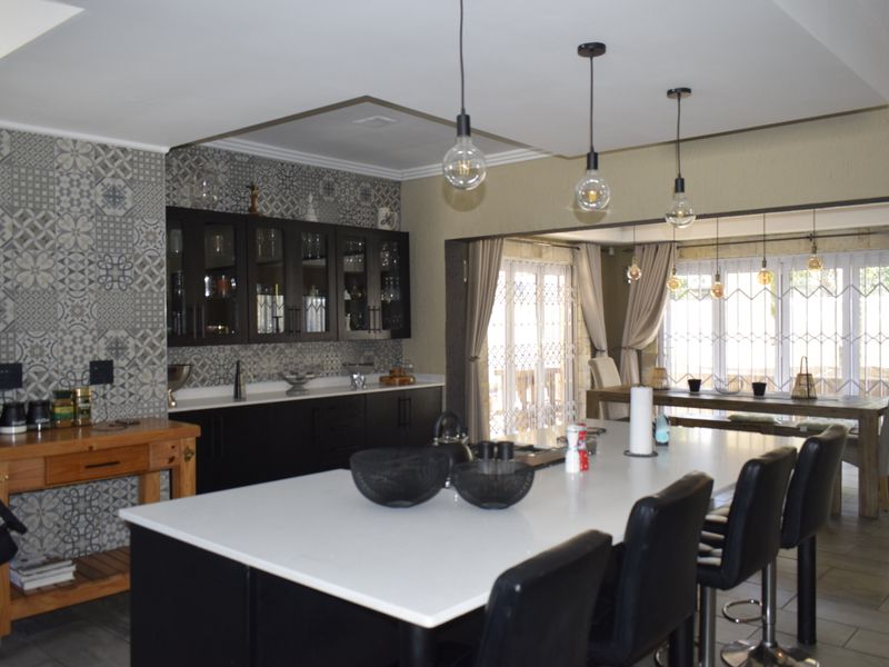 Spacious open-plan kitchen featuring a large island with quartz countertops, dark cabinetry, and decorative tiled backsplash, flowing into a bright dining area.