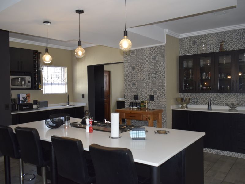 Modern kitchen featuring a large central island with quartz countertops, dark cabinetry, decorative tile backsplash, and stylish pendant lighting.