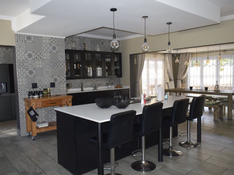 Modern open-plan kitchen featuring a large central island, dark cabinetry, patterned feature wall, and contemporary pendant lighting, seamlessly flowing into the dining area.