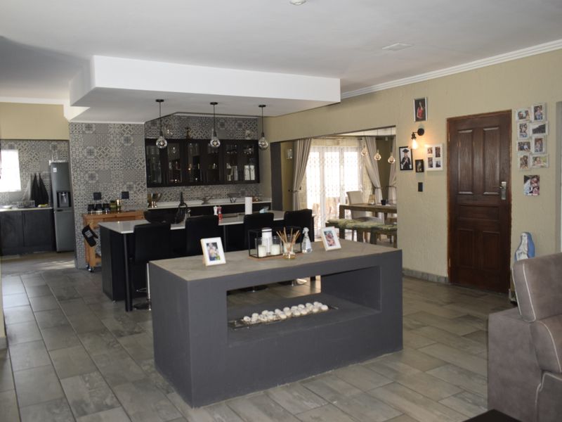 Spacious open-plan living area featuring a modern kitchen with island, tiled flooring, and a central fireplace, creating a functional and connected family space.