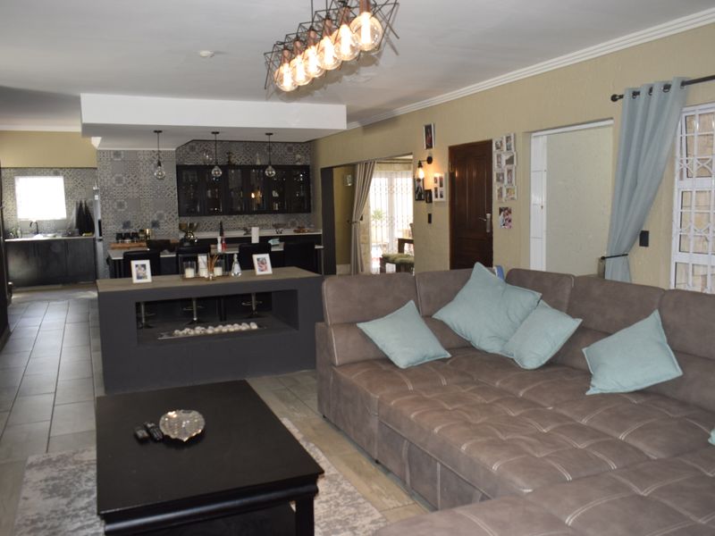 Spacious open-plan living area featuring a modern kitchen with decorative tiling, a central island, and a built-in fireplace, seamlessly connecting to the lounge.