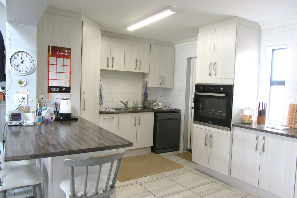 A functional kitchen featuring light-toned cabinetry, a built-in oven, integrated dishwasher space, tiled flooring, and a breakfast bar counter.