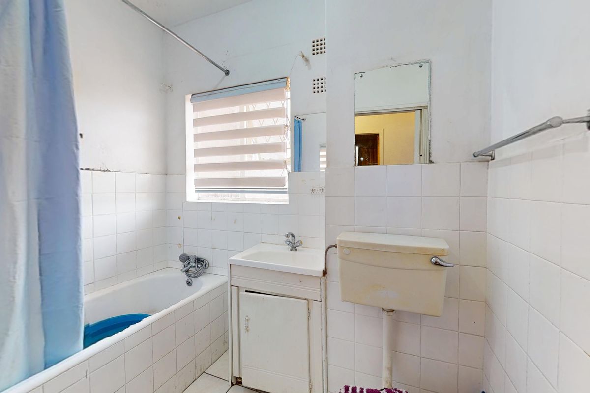 A dated bathroom featuring a bathtub, wall-mounted toilet cistern, and vanity basin with tiled finishes, requiring cosmetic updates and modernization.