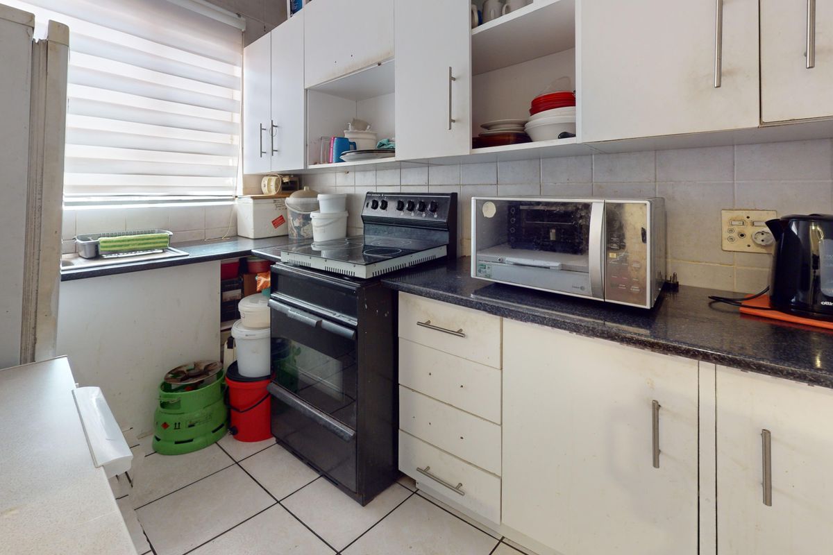 A compact kitchen featuring white cabinetry, dark laminate countertops, tiled backsplash, and a freestanding oven, offering potential for a modern update.