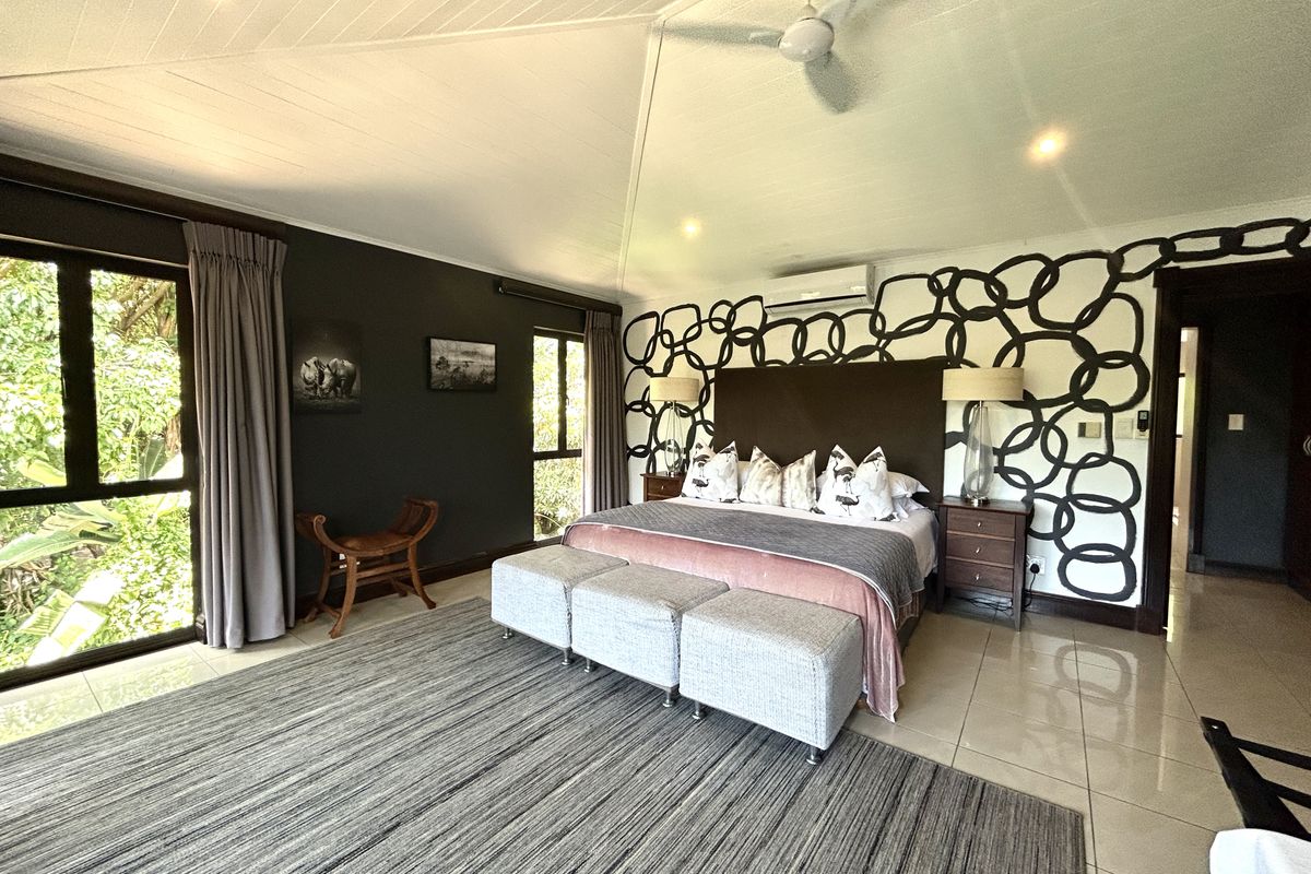 Spacious bedroom featuring a vaulted ceiling, ceiling fan, split-system air conditioning, and large windows providing natural light and garden views.