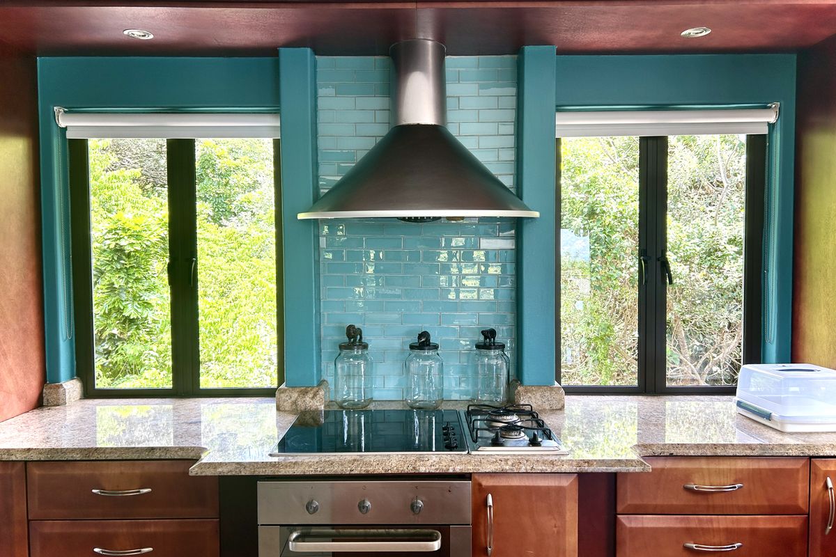 A well-maintained kitchen featuring granite countertops, a dual electric and gas cooktop, stainless steel extractor fan, and vibrant teal subway tile backsplash.