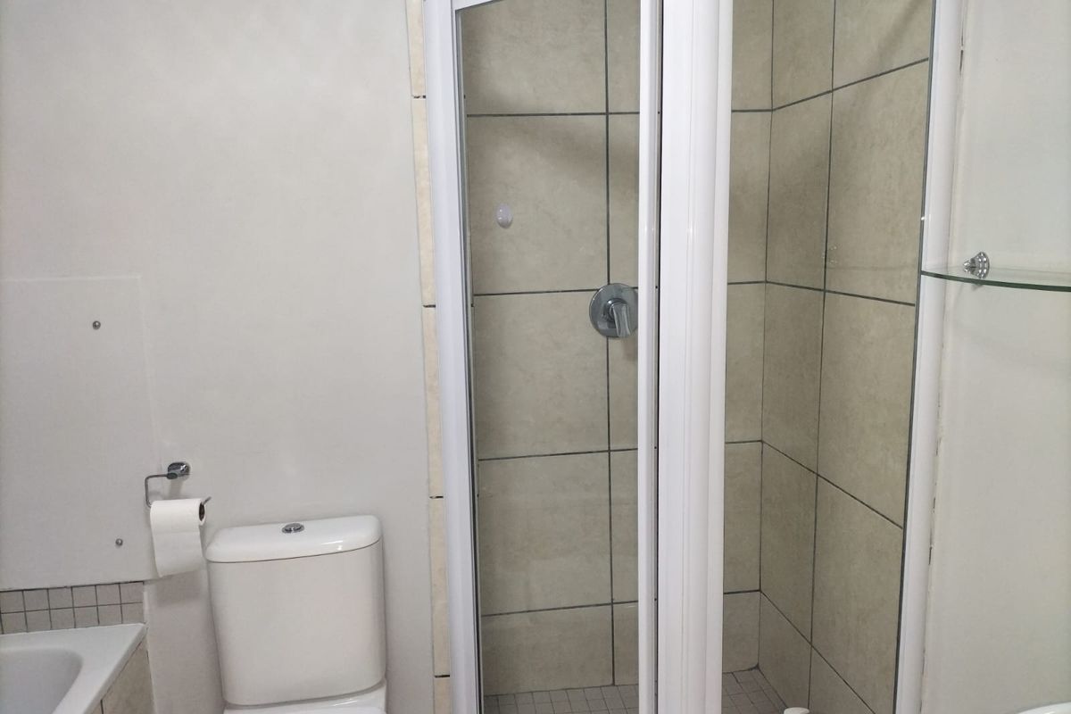 A functional bathroom featuring a tiled shower enclosure with a glass door, a standard toilet, and neutral wall finishes.