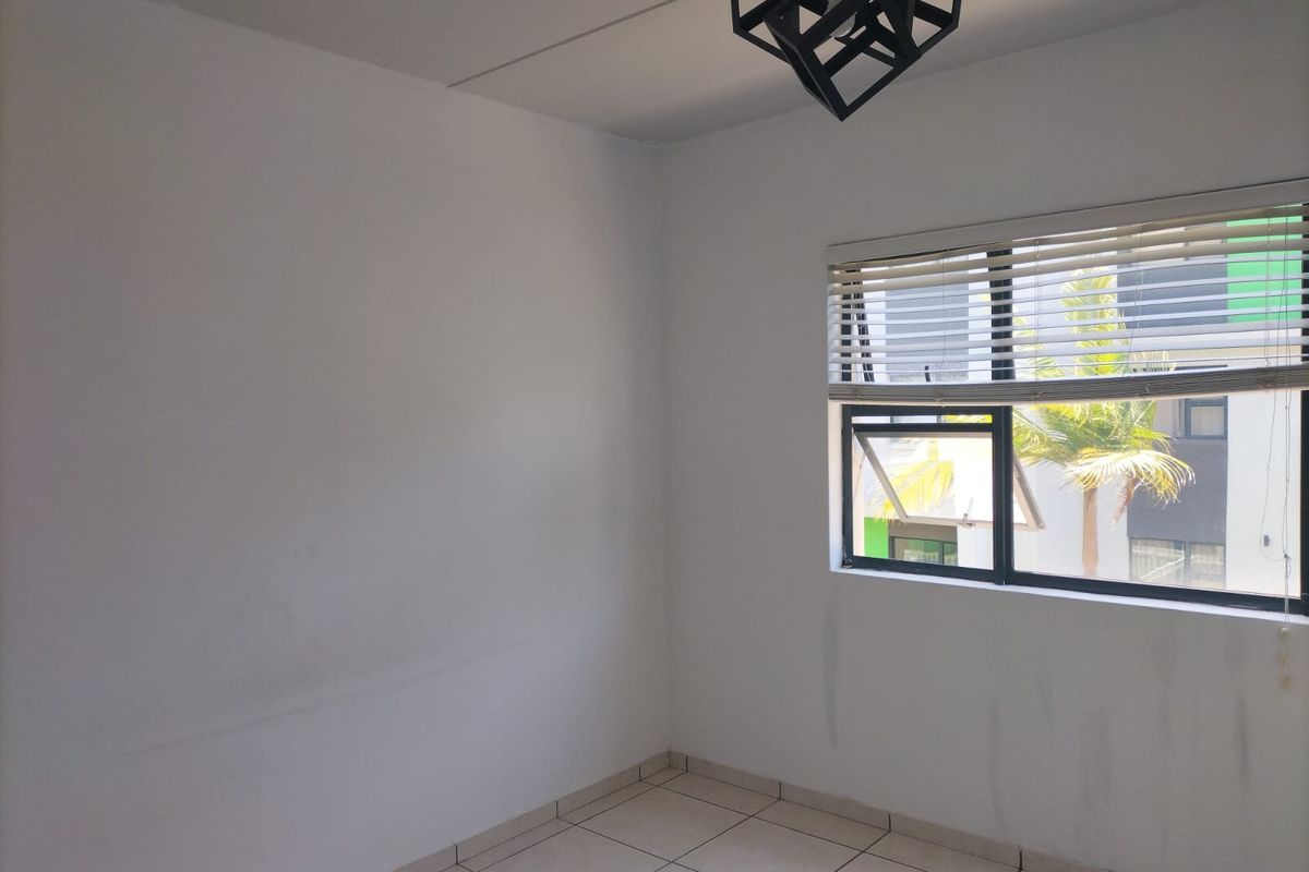 An empty bedroom featuring tiled flooring, a modern geometric light fixture, and venetian blinds, providing a neutral canvas for personalization.