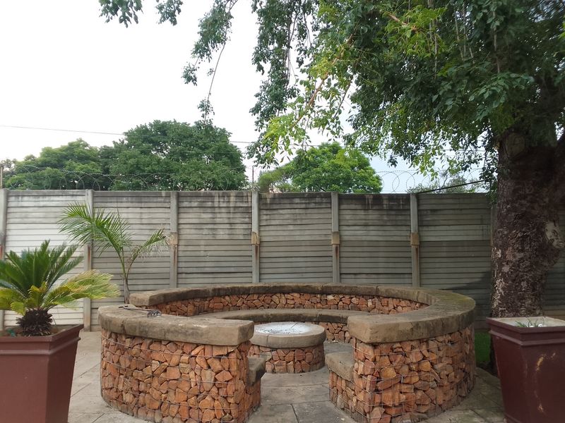 Outdoor garden area featuring a circular gabion stone fire pit, paved flooring, and a secure precast concrete boundary wall with razor wire.