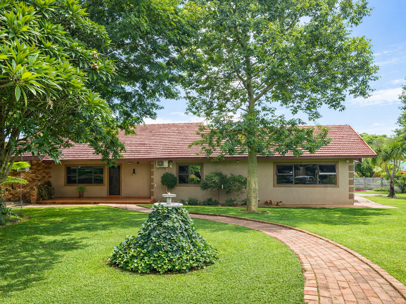 A well-maintained single-story home featuring a classic tiled roof, brick facade, and a beautifully landscaped front garden with a winding brick pathway.