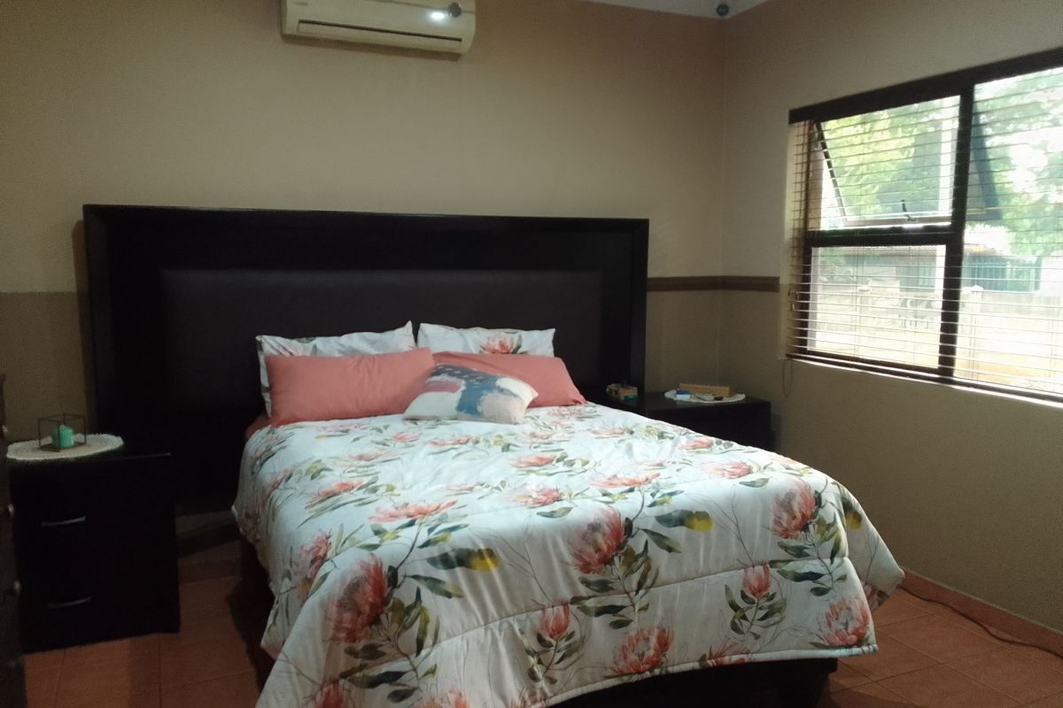 A bedroom featuring tiled flooring, a wall-mounted air conditioning unit, and venetian blinds on the window.