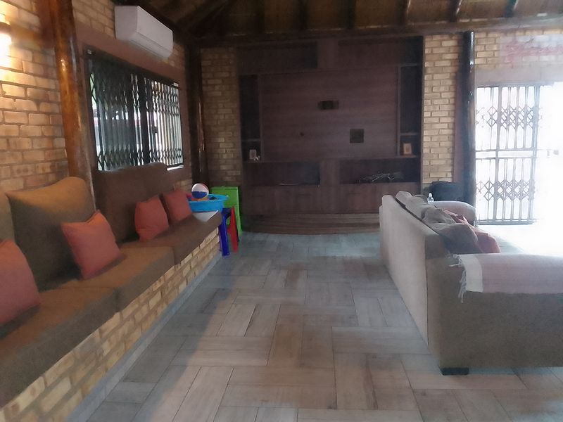 Spacious living area featuring exposed brick walls, timber ceiling beams, tiled flooring, and a large built-in wooden entertainment unit.