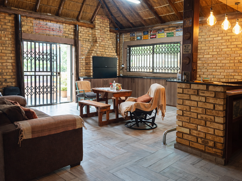 Open-plan living area featuring exposed brick walls, a traditional thatched roof, and a built-in braai, creating a rustic and cozy entertainment space.