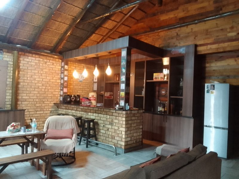 A rustic-style indoor bar area featuring a brick-based counter, timber-clad vaulted ceiling, and integrated cabinetry with warm pendant lighting.