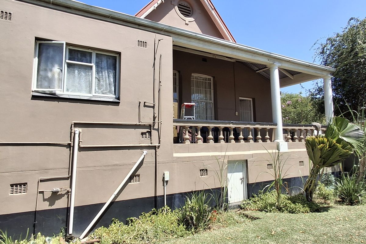 Rear elevation of the apartment building featuring a covered patio with a balustrade, external plumbing, and established garden surroundings.