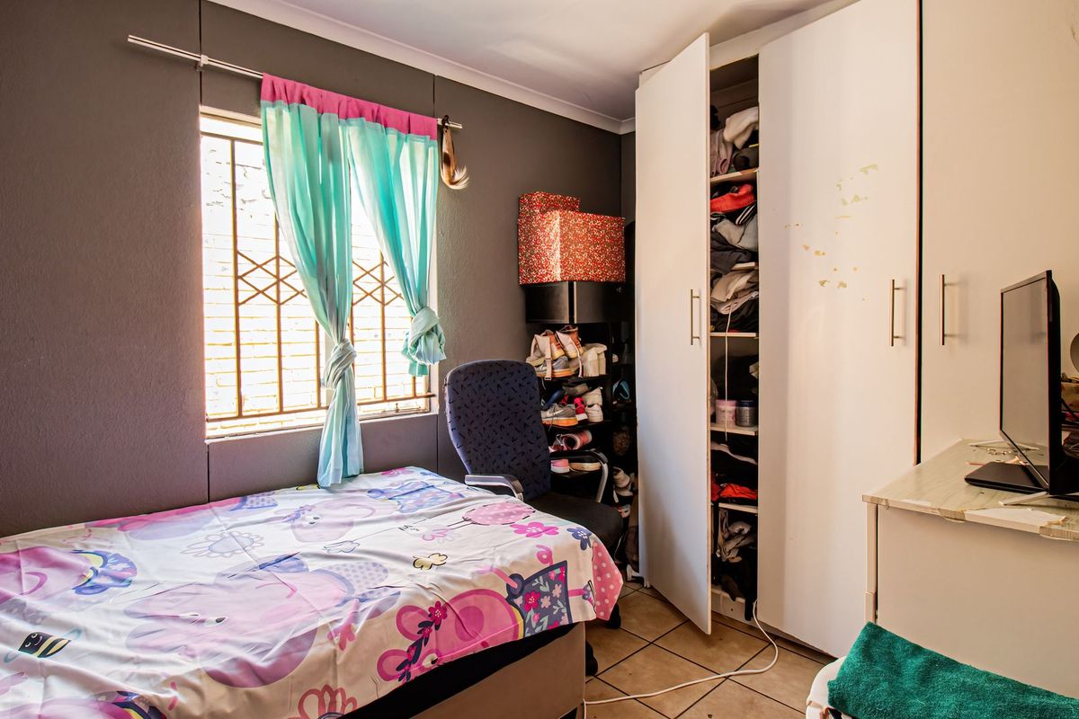 A functional bedroom featuring tiled flooring, a built-in wardrobe, and security bars on the window.