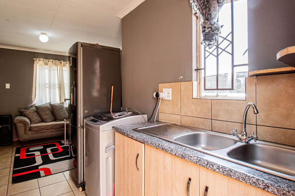 Compact kitchen area featuring laminate cabinetry, a double bowl stainless steel sink with mixer tap, and tiled splashback, with an adjacent living space.
