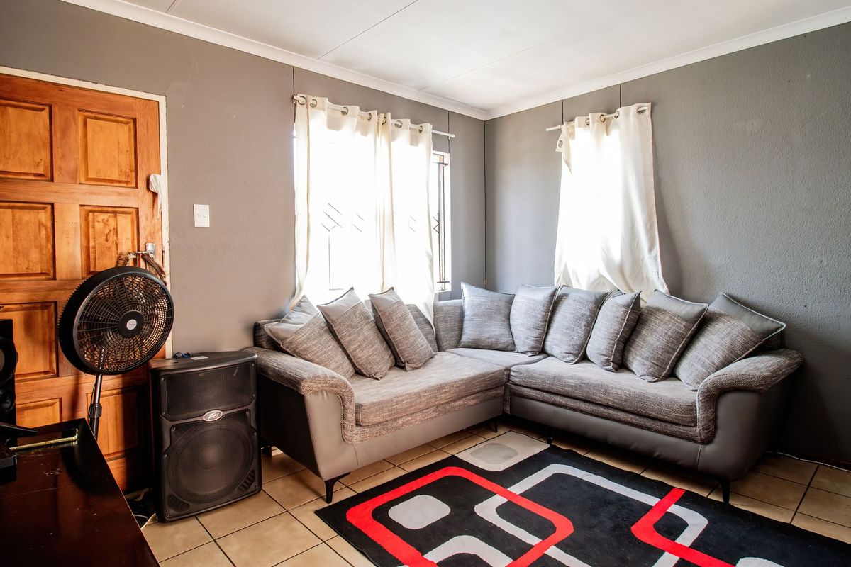 A cozy living room featuring tiled flooring, a timber door, and natural light through windows fitted with security bars.