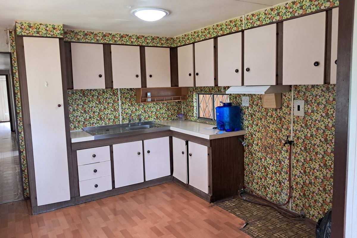 A dated kitchen featuring original cabinetry, laminate countertops, and retro floral wallpaper, offering a blank canvas for a modern renovation.
