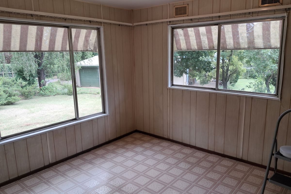 A vacant living area featuring dated vertical wall paneling, vinyl flooring, and large windows with external awnings overlooking the garden.