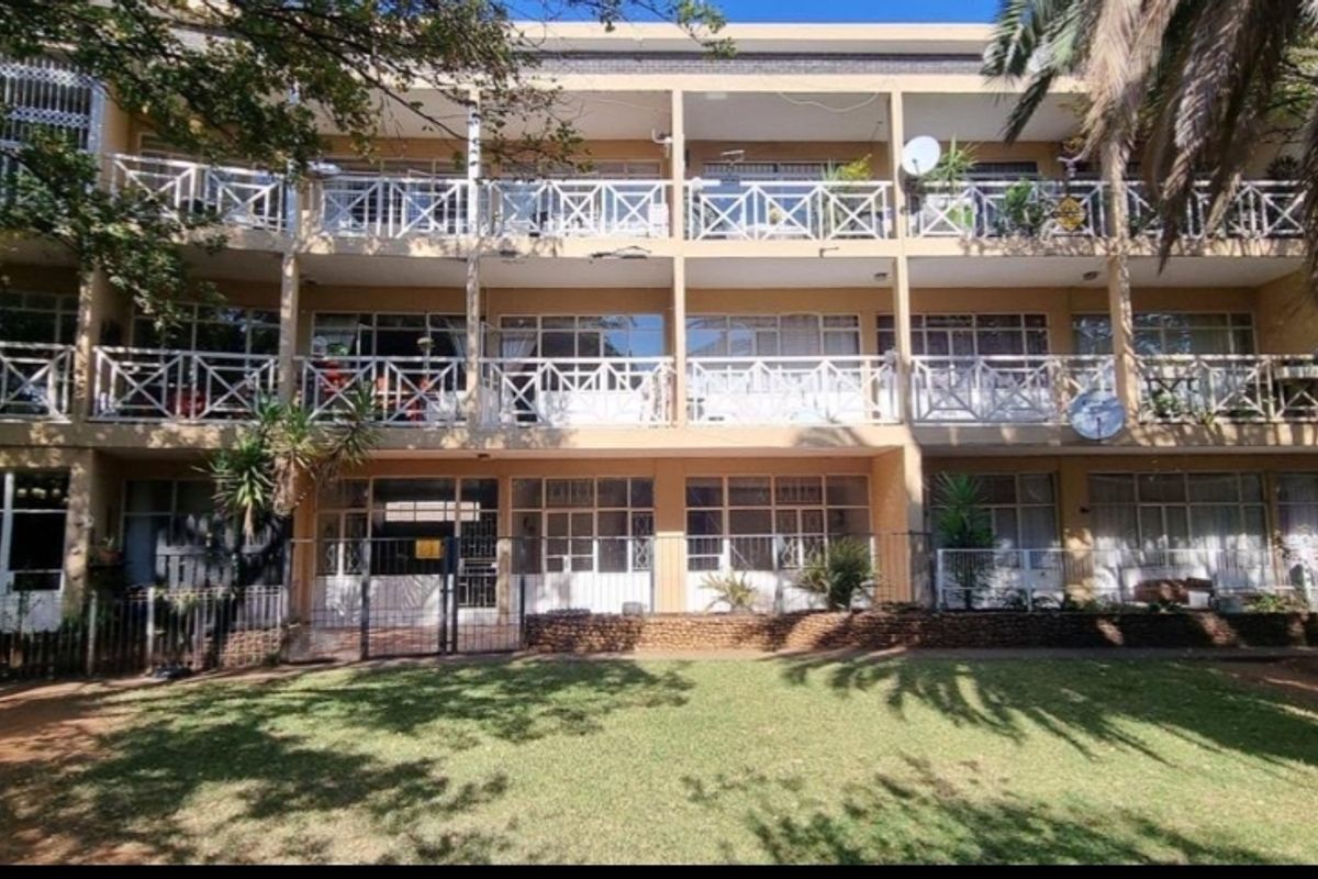 Rear elevation of a multi-story apartment complex featuring private balconies with metal railings, sliding glass doors, and access to a communal garden area.