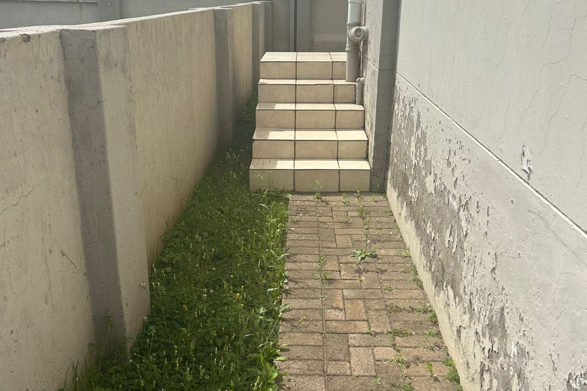 Side exterior walkway featuring paved path, tiled steps, and perimeter boundary wall with security fencing.