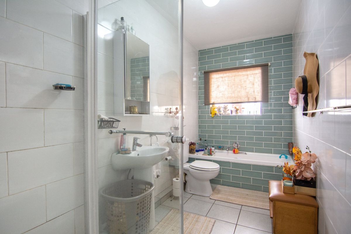 A well-maintained bathroom featuring a glass shower enclosure, a bathtub with green subway tile surround, a wall-mounted basin, and a medicine cabinet.