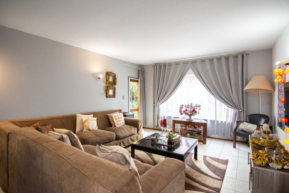 A comfortable living room featuring neutral tiled flooring, soft wall lighting, and a glass-paneled door providing natural light and access to the exterior.