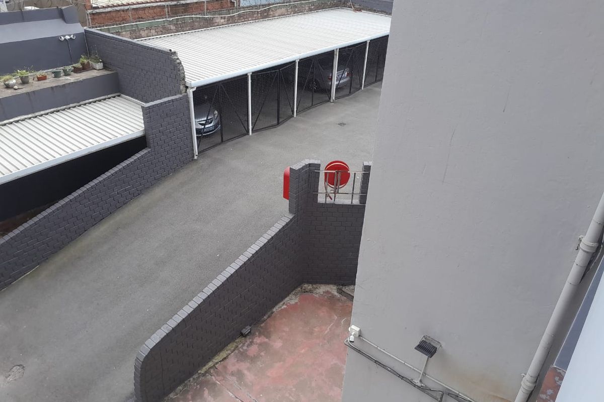 Elevated view of the apartment complex rear area, featuring a paved driveway, covered carport parking bays, and a brick boundary wall.