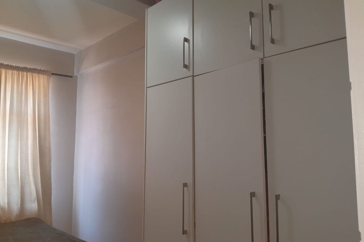 A bedroom featuring white built-in cupboards with modern handles and a window with curtain fittings.