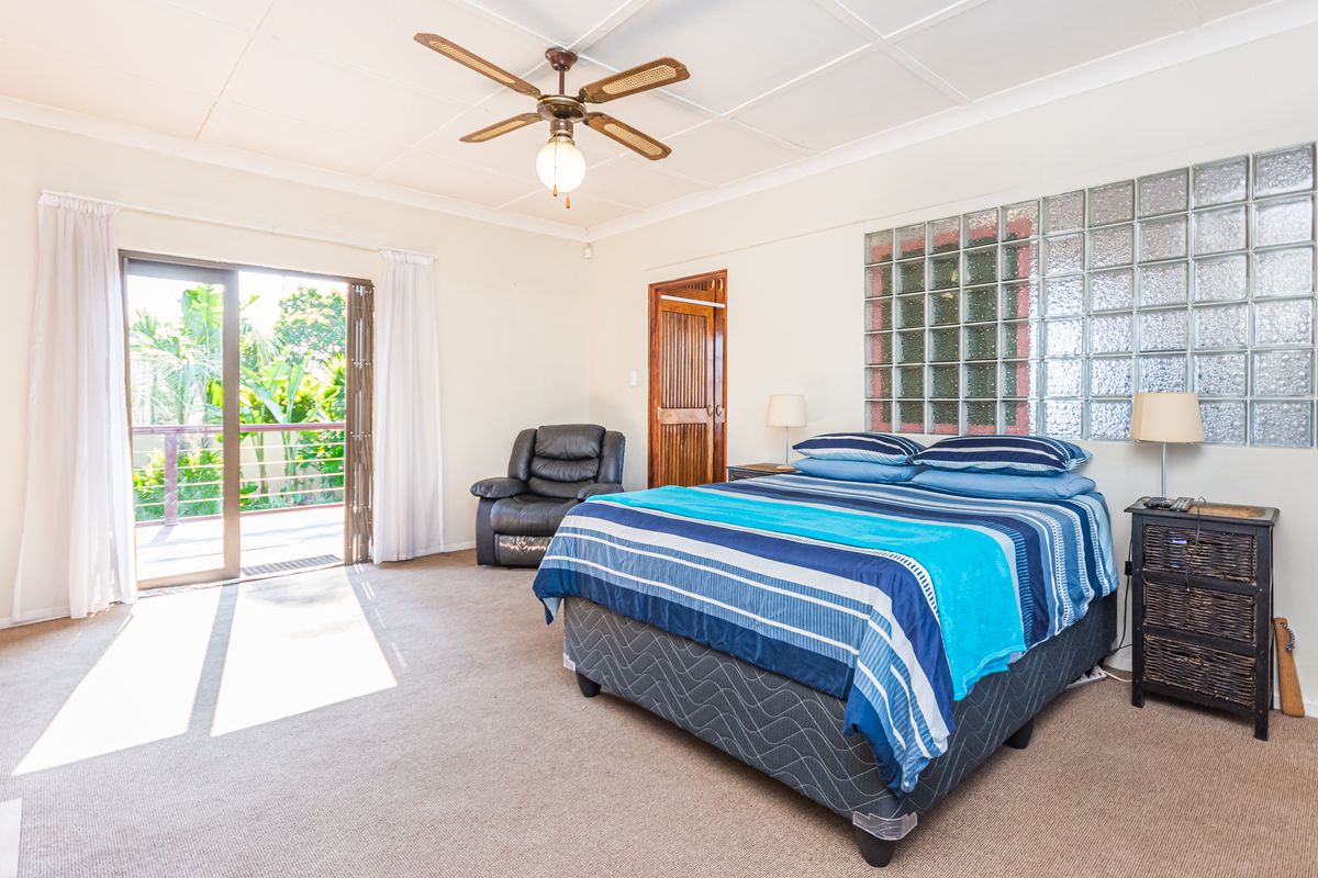 Spacious bedroom featuring a glass block feature wall, ceiling fan, and sliding door access to an outdoor balcony area.
