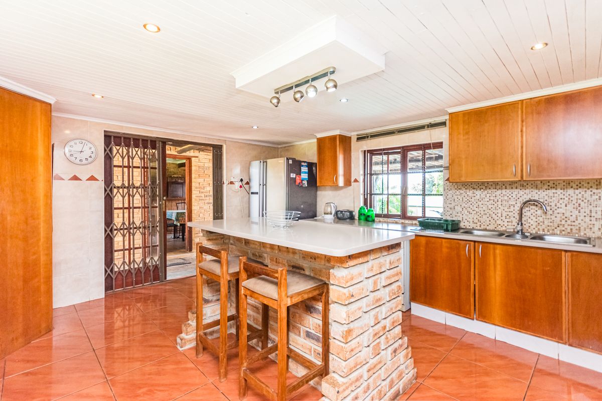 A functional kitchen featuring wooden cabinetry, a brick-based breakfast island, tiled flooring, and a mosaic tile backsplash with recessed ceiling lighting.