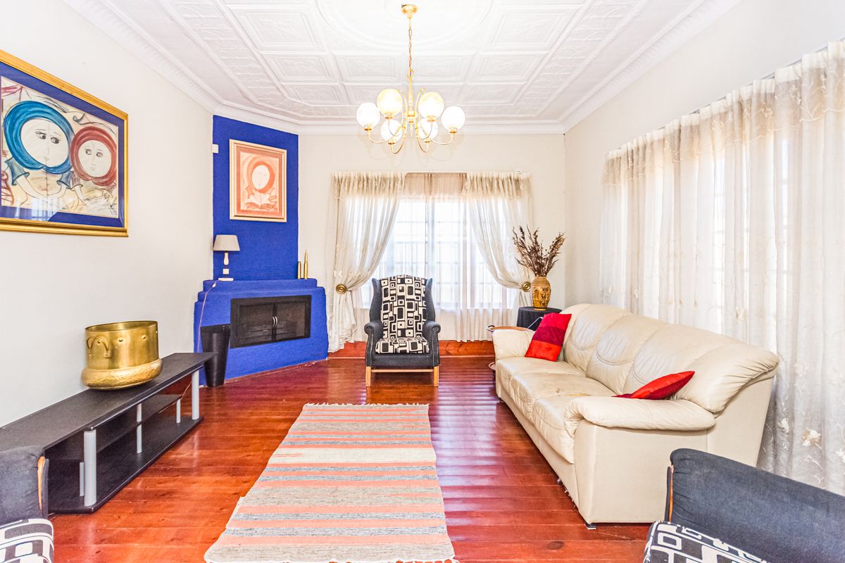 A living room featuring original timber flooring, a decorative pressed ceiling, and a corner fireplace with a bold blue finish.
