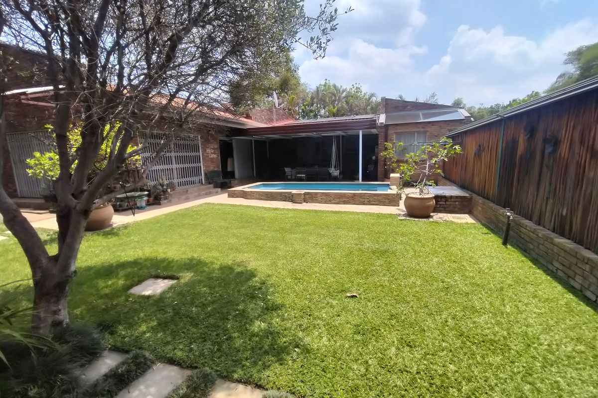 Rear garden featuring a swimming pool, covered patio area, and established lawn, enclosed by brick and timber boundary fencing.
