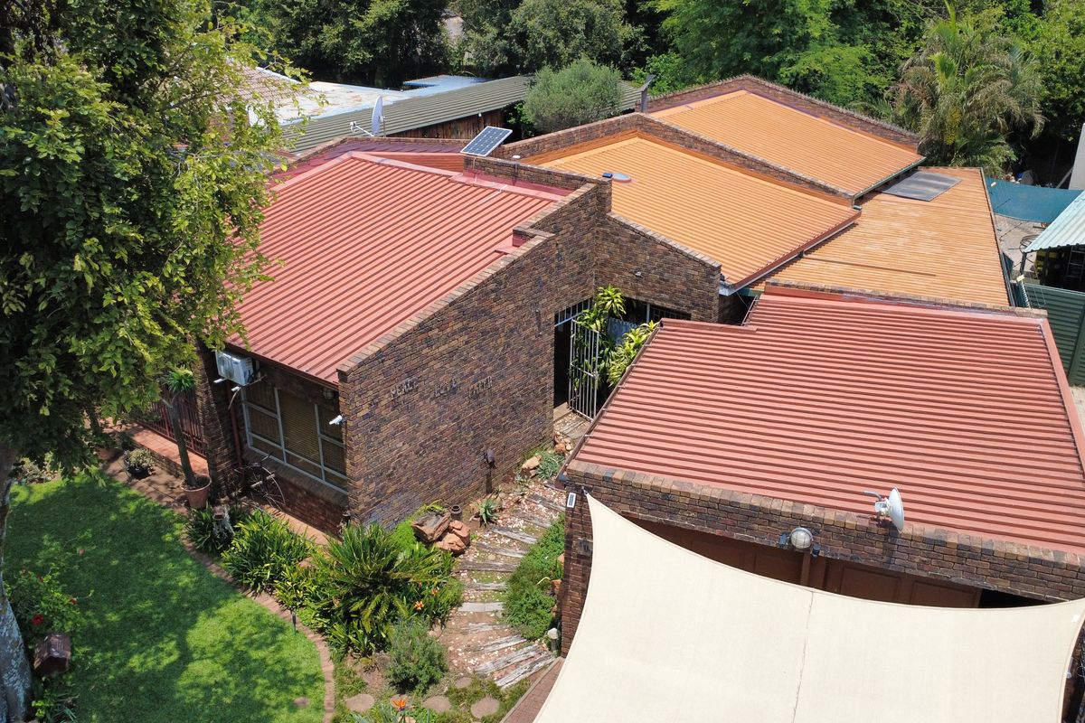 Aerial view of the property showcasing the face brick exterior, corrugated metal roofing, and surrounding garden area with a paved walkway.