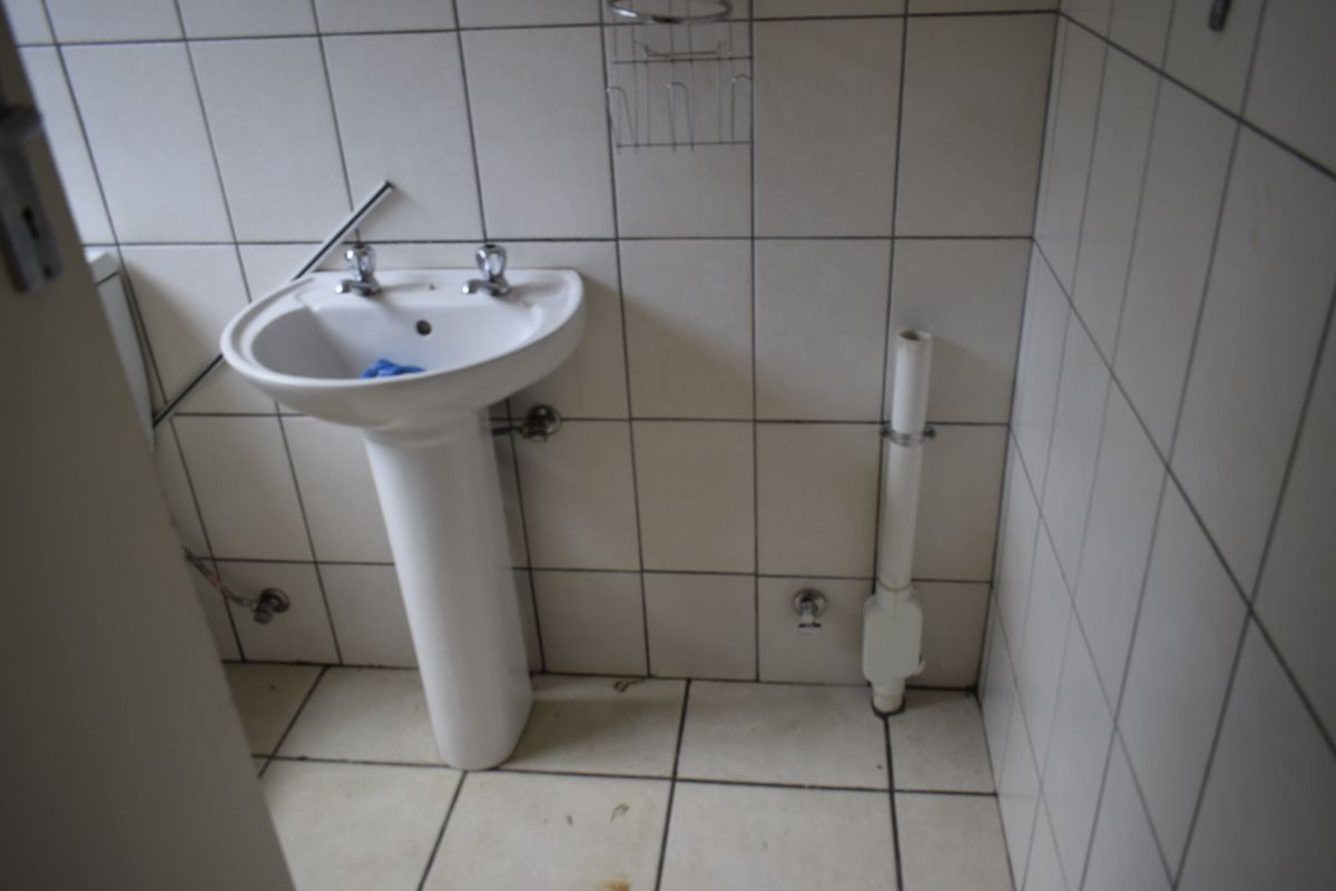 A small bathroom featuring a pedestal basin and fully tiled walls and floors, currently requiring cosmetic updates and plumbing finishing.