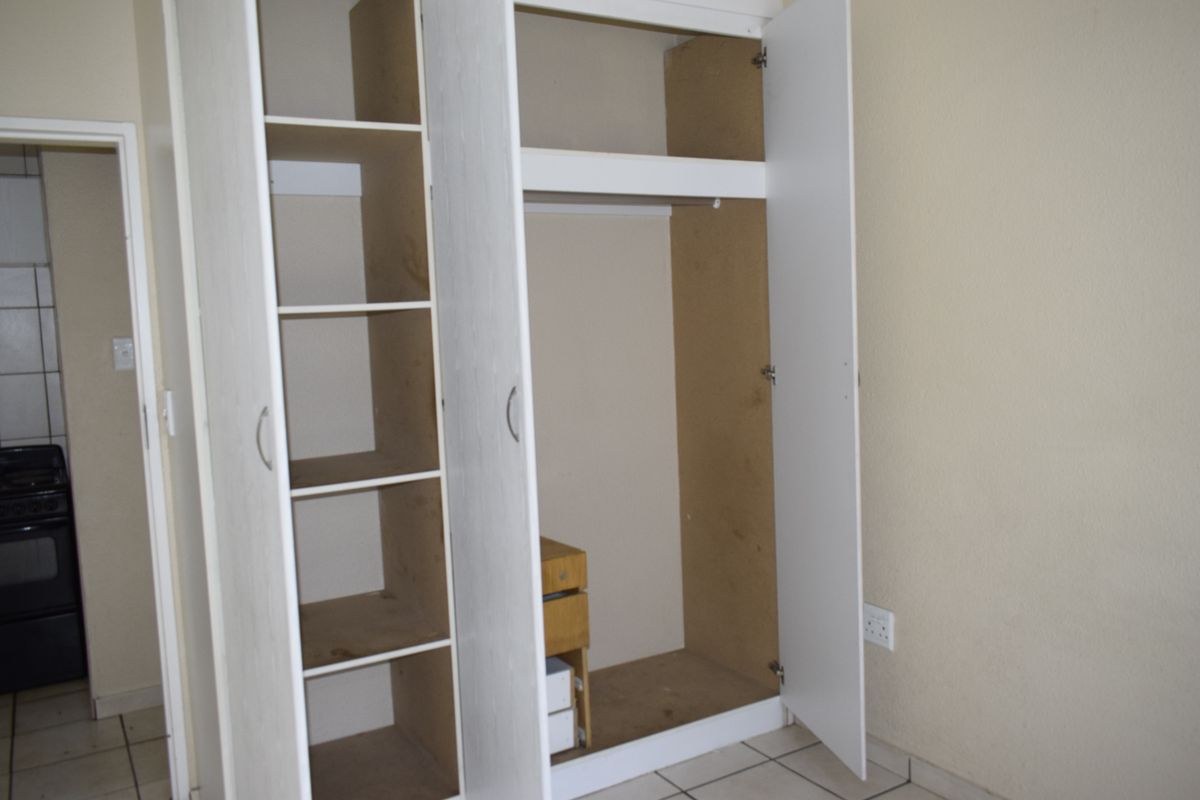 A bedroom featuring a built-in wardrobe with shelving and hanging space, finished with tiled flooring and neutral wall paint.