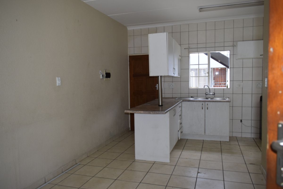 A functional kitchen space featuring tiled flooring, a tiled backsplash, and basic cabinetry with a breakfast bar counter, awaiting modern updates.