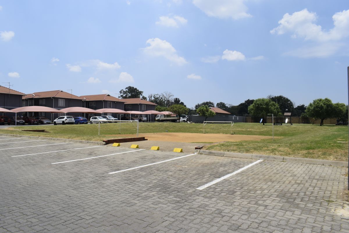 View of the townhouse complex exterior featuring a paved parking area, covered carports, and a communal recreational lawn space.