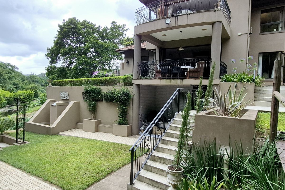 Rear view of the property featuring a multi-level garden, concrete staircase with wrought iron railings, and a covered patio area with balcony above.