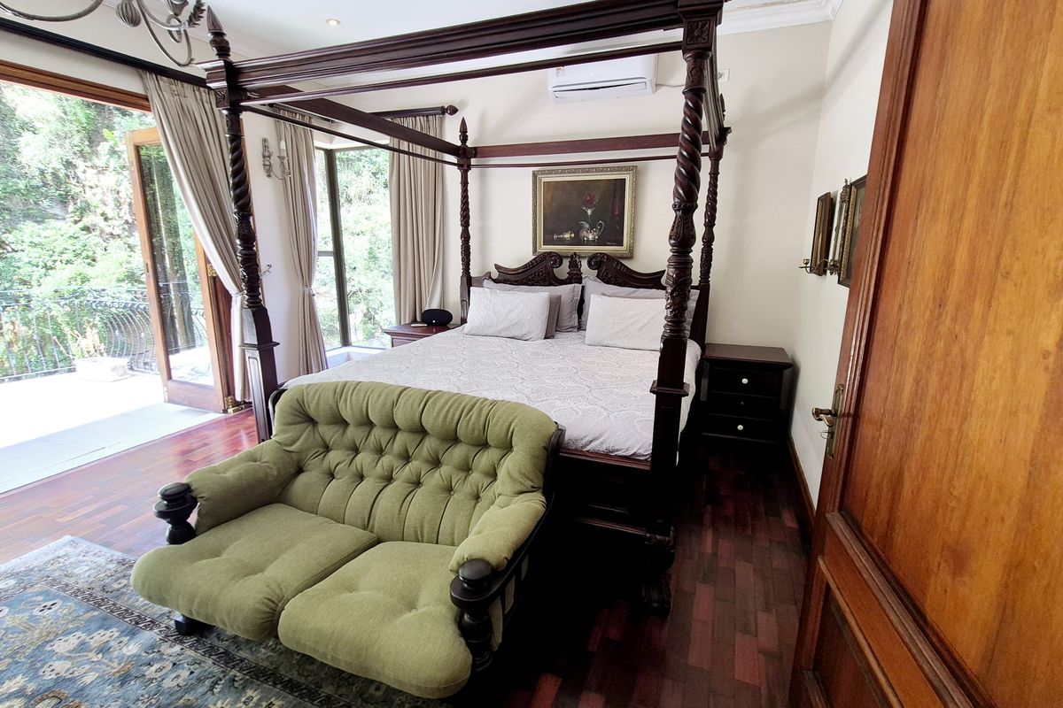 Spacious bedroom featuring rich hardwood flooring, crown molding, a split-system air conditioner, and direct access to a private balcony through elegant french doors.