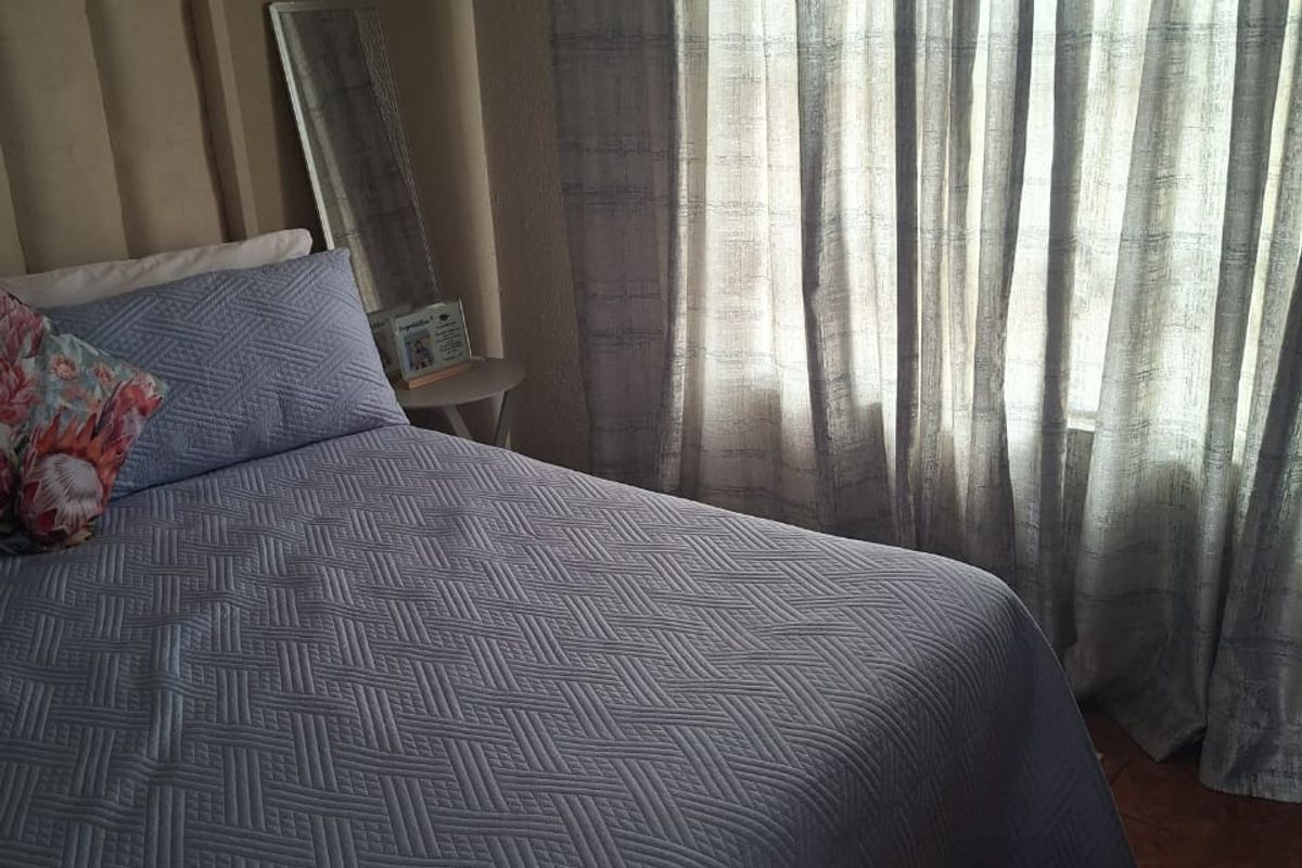 A cozy bedroom featuring tiled flooring and natural light filtered through window curtains.
