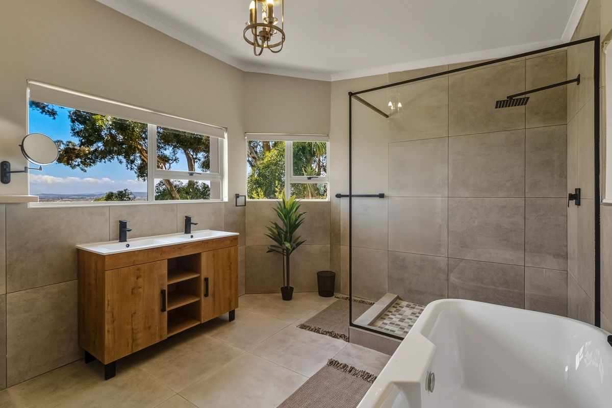 Modern bathroom featuring a double vanity, walk-in shower with black matte fixtures, and a freestanding bathtub with scenic window views.