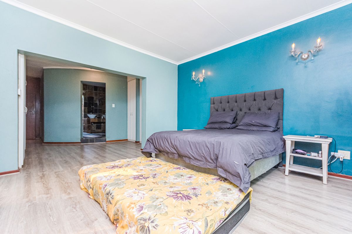 Spacious bedroom featuring laminate flooring, bold accent walls, wall sconce lighting, and an adjoining en-suite bathroom area with built-in storage.