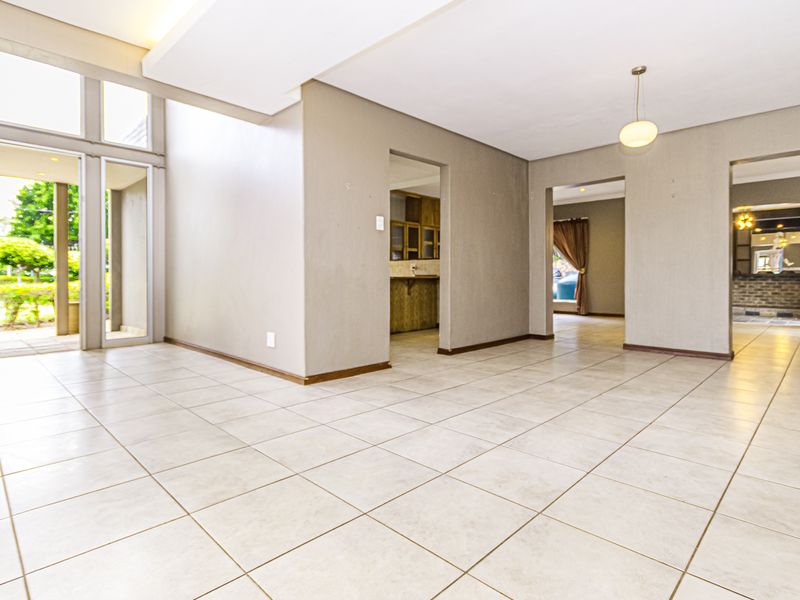 Spacious, light-filled living area featuring neutral tiled flooring, high ceilings, and large glass doors providing seamless access to the outdoor garden space.