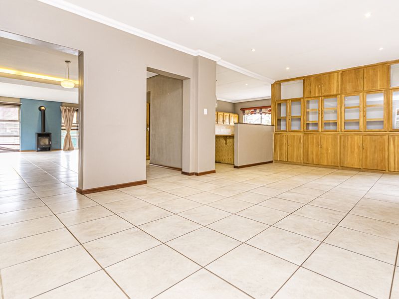 Spacious open-plan living area featuring neutral tiled flooring, extensive built-in wooden cabinetry, and a cozy wood-burning fireplace in the adjacent room.