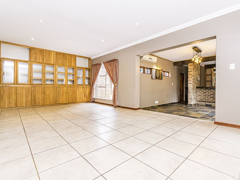 Spacious open-plan living area featuring large built-in wooden cabinetry, tiled flooring, and an adjoining bar area with brick accents and slate flooring.